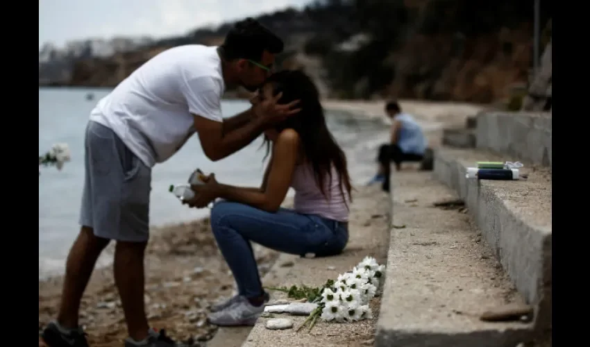 Un hombre besa a su hermana mientras un ramo de flores yace en el lugar donde un bebé de seis meses perdió la vida tras el incendio forestal de Mati. Foto: EFE